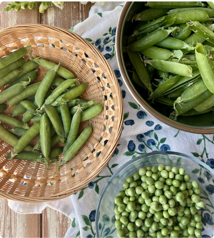 Fresh pea pods in a woven basket beside a bowl of shelled peas