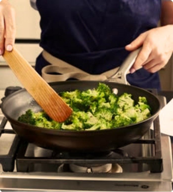 Broccoli being stirred in a skillet on a stovetop